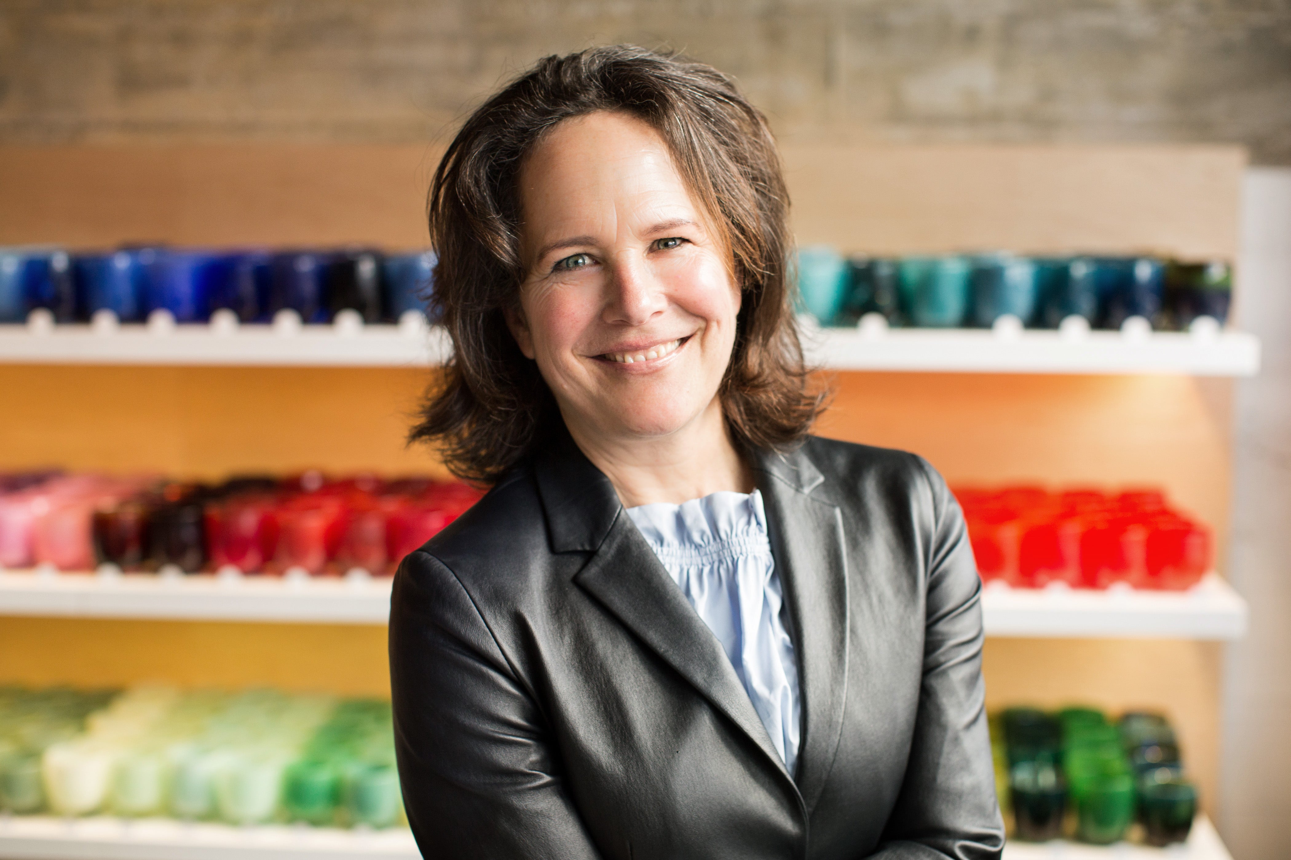 Lee Rhodes, glassybaby founder smiling in front of various glassybaby in a glassybaby retail store.