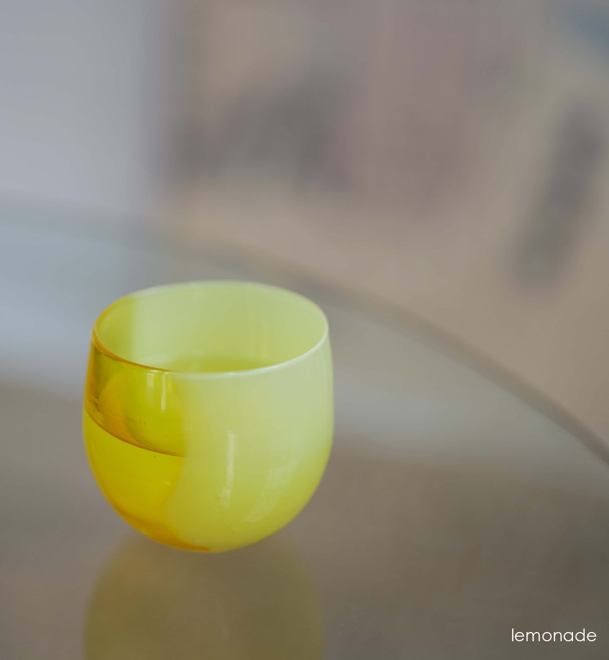 lemonade vibrant yellow, hand-blown drinking glass with liquid inside on a reflective blurred surface.