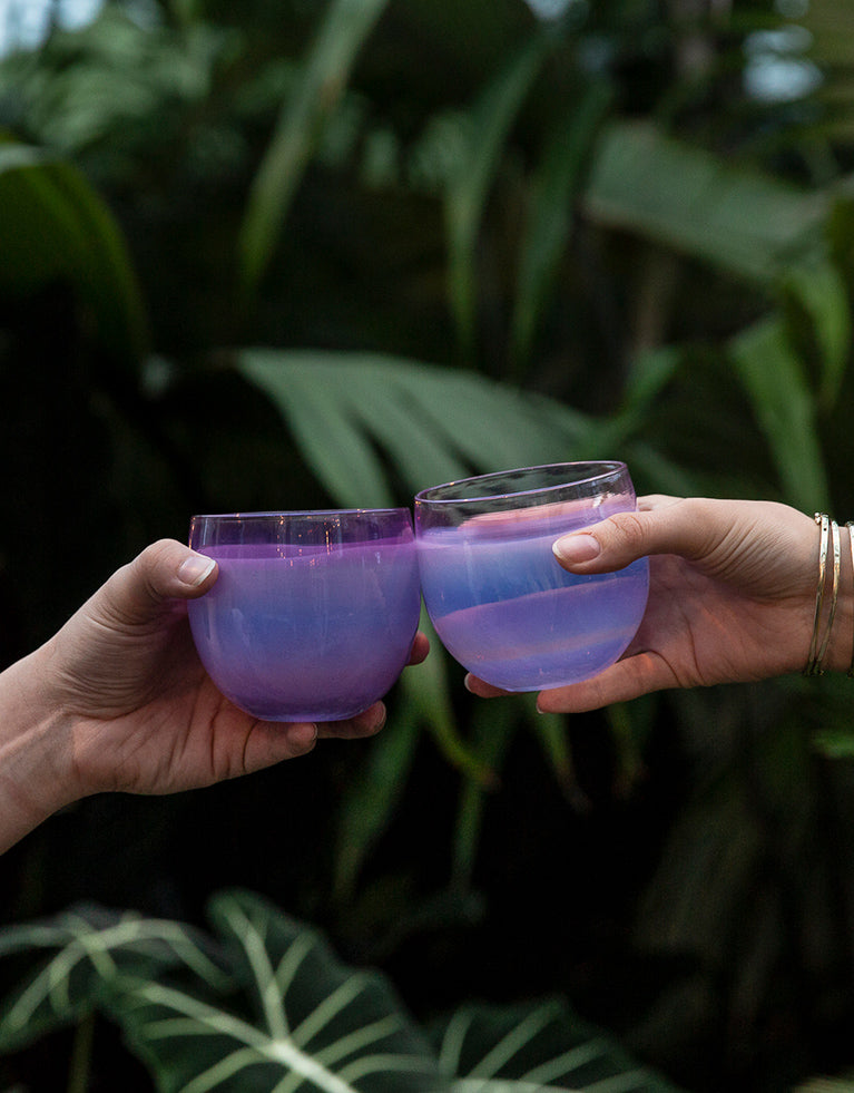2 mama drinkers being cheersed outside. hand-blown glass drinking glasses in a beautiful purple hue.
