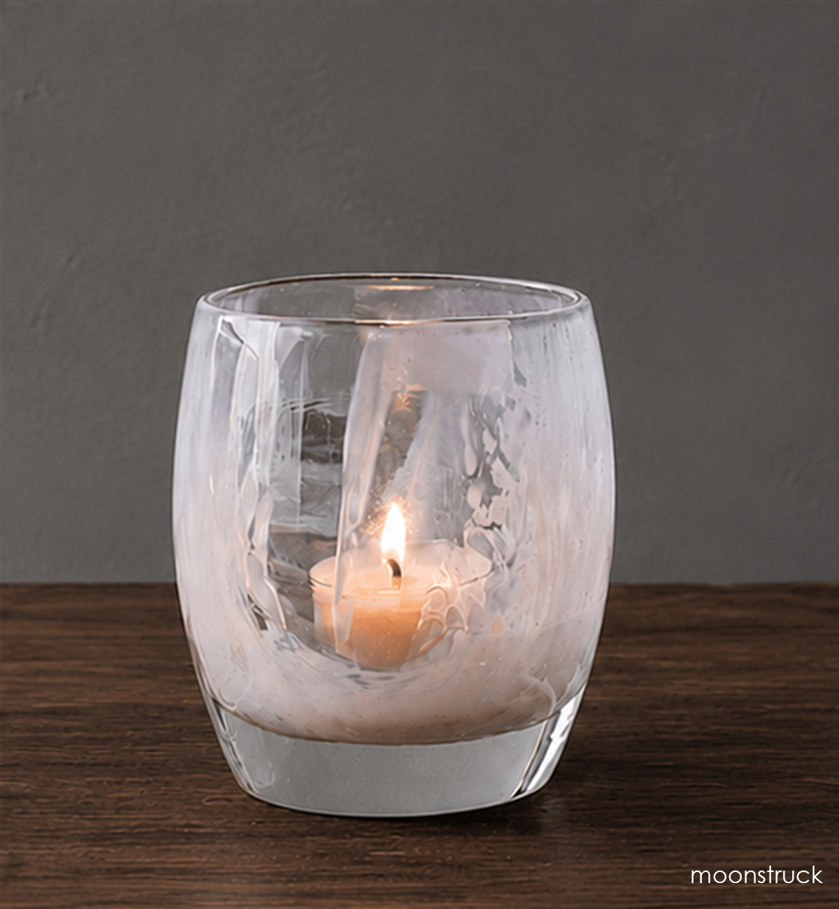 Clear glass candle holder with a lit candle on a wooden surface and dark background