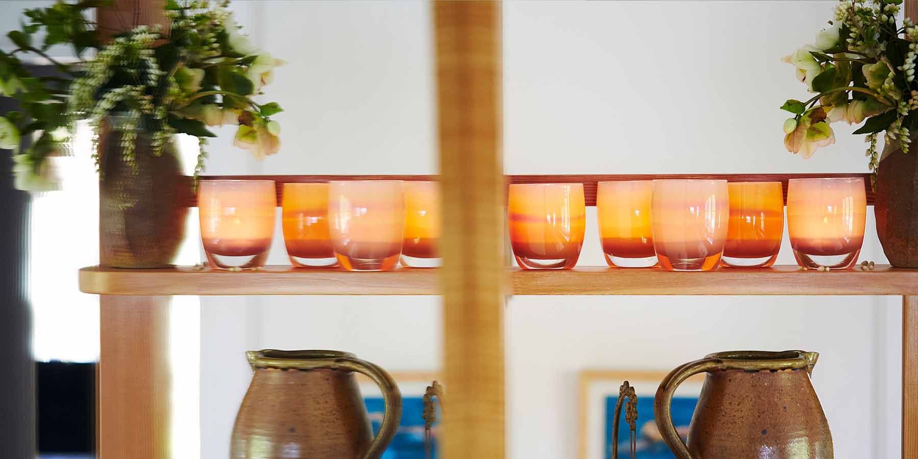 nurture, warm peachy with purple banding, hand-blown glass votive candle holder lined up on a shelf.
