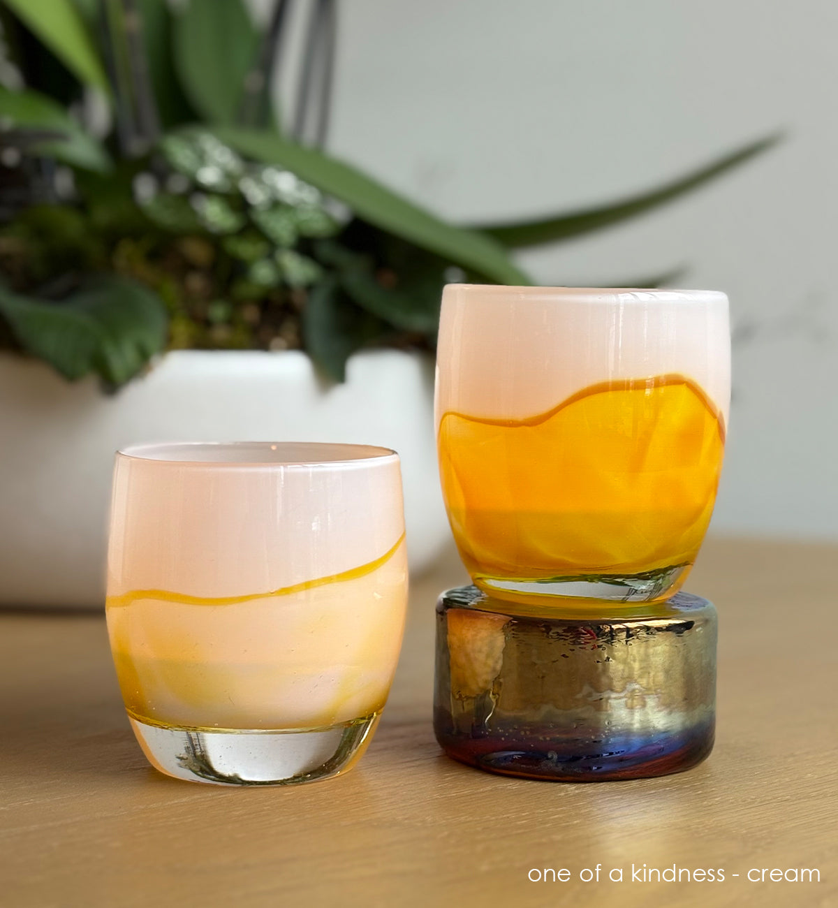 Two yellow and cream coloration glass candle holders  on a wooden surface with a plant in the background.