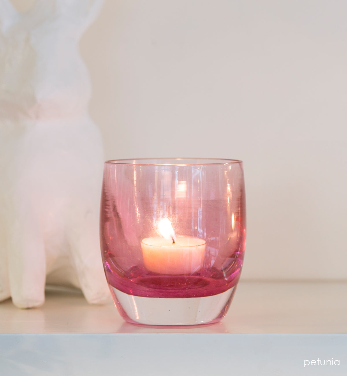 petunia transparent light pink hand-blown glass votive candle holder with white bunny behind it.