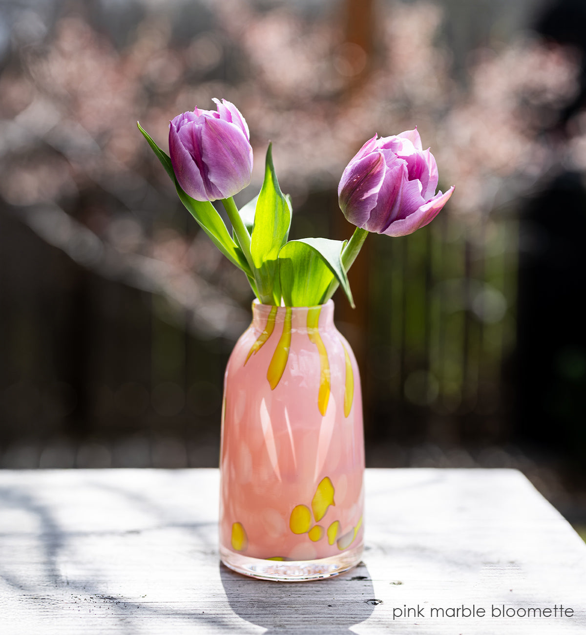 Pink marble-patterned bloomette vase with purple tulips on a wooden surface