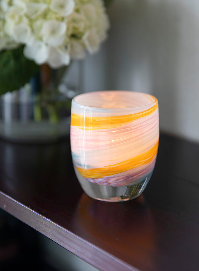 places you'll go multi-colored yellow, white, blue, purple hand-blown glass votive candle holder sitting on dark wood table in front of a flower vase.