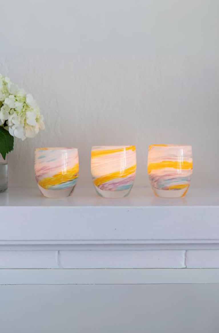 three places you'll go multicolored yellow, white, purple and blue hand-blown glass votive candle holders, placed on a white mantle next to flower vase.