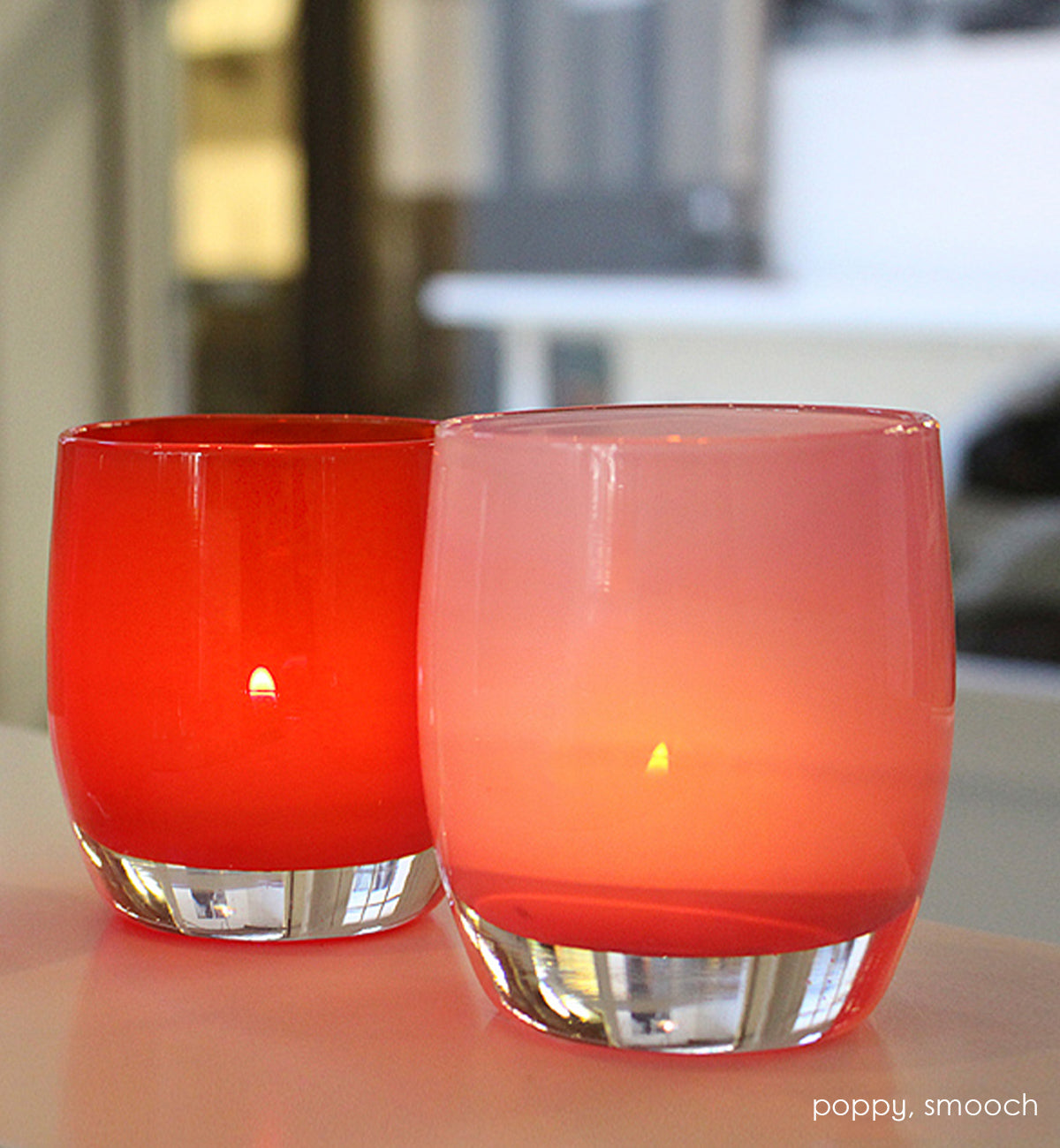 poppy red hand-blown glass votive candle holder with smooch on a dark cream counter.