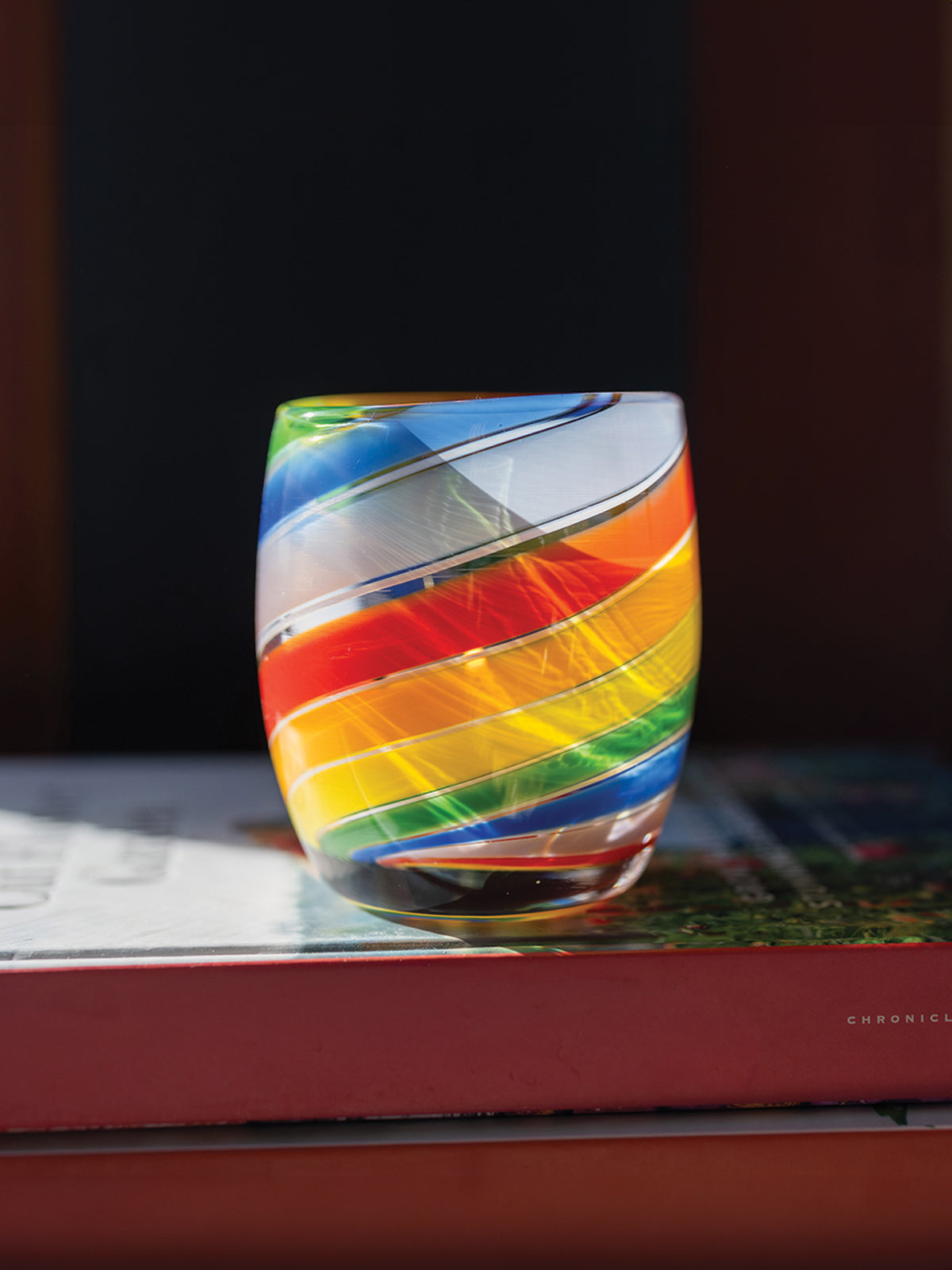 'pride 2025' glassybaby with rainbow swirls, hand-blown glass candle holder sitting on a book
