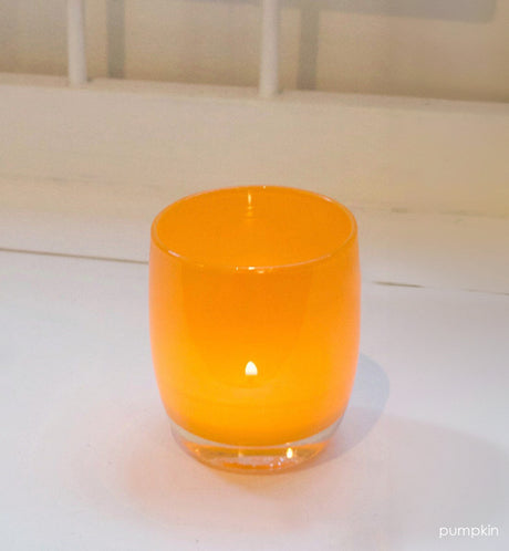 pumpkin orange hand-blown glass votive candle holder with a lit tealight on a white surface.