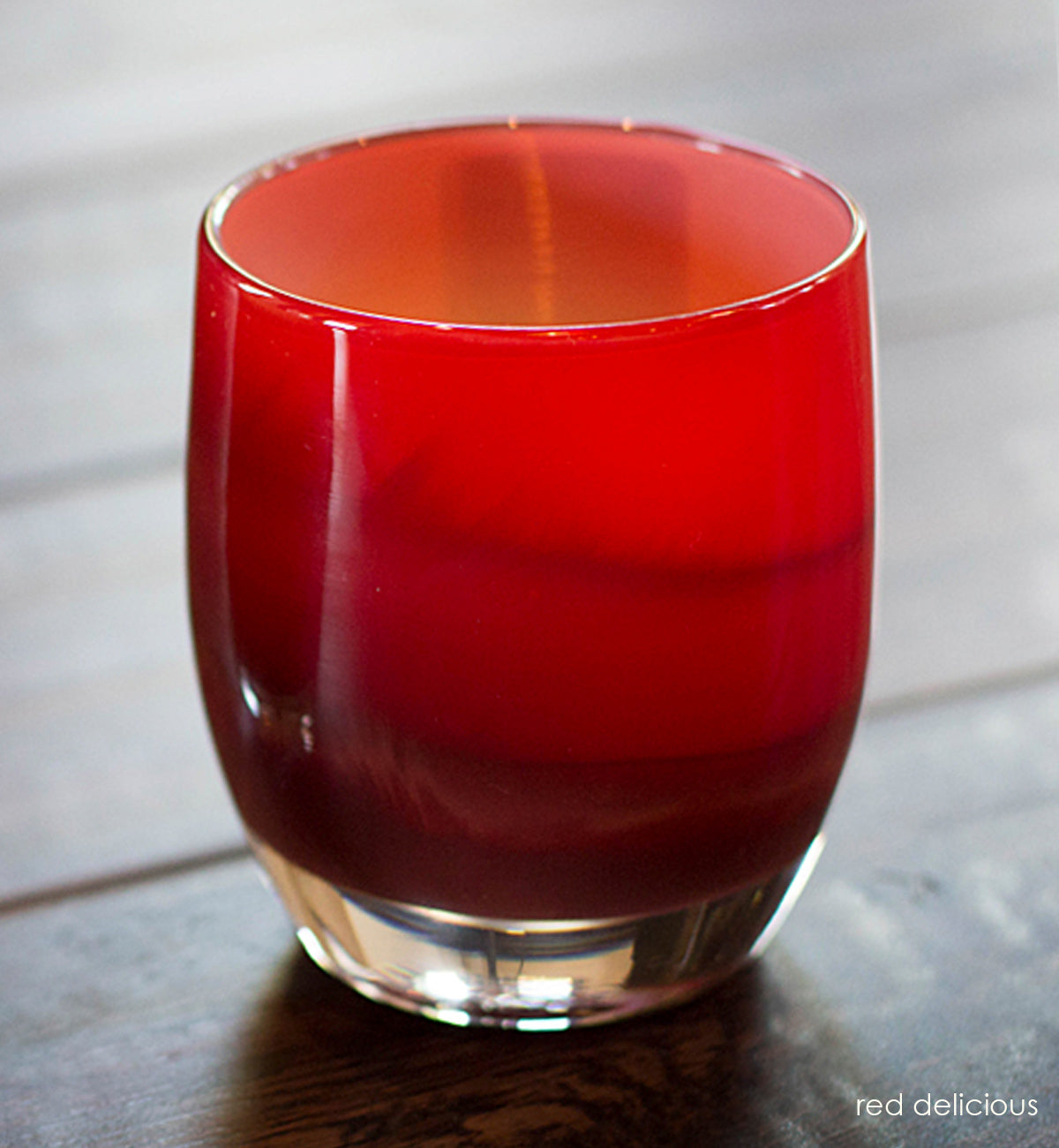 red delicious, bright red with a stark white interior hand-blown glass votive candle holder glowing with a lit tealight on a dark wood surface.