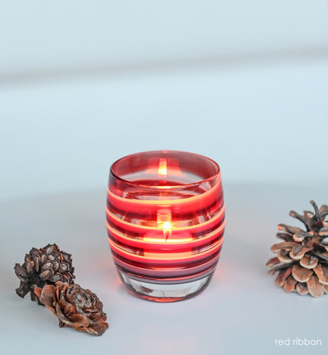 red ribbon red white swirl hand-blown glass votive candle holders on a cream surface next to decorative pinecones.