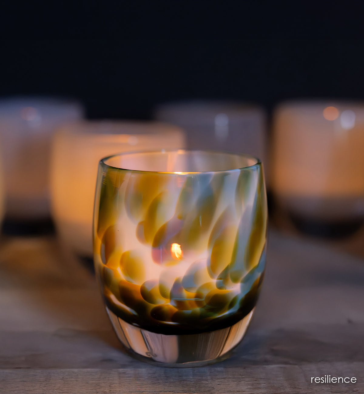 resilience | white hand-blown glass candle holder with brown, blue, and green petal deign with a lit candle on a wooden surface