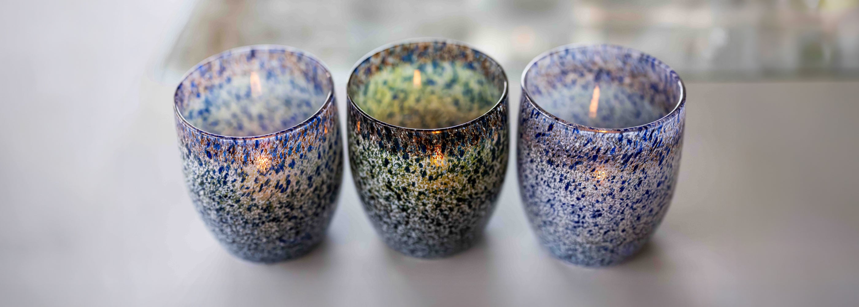 Three speckled blue, white and green ceramic candle holders with lit candles inside on a light background.