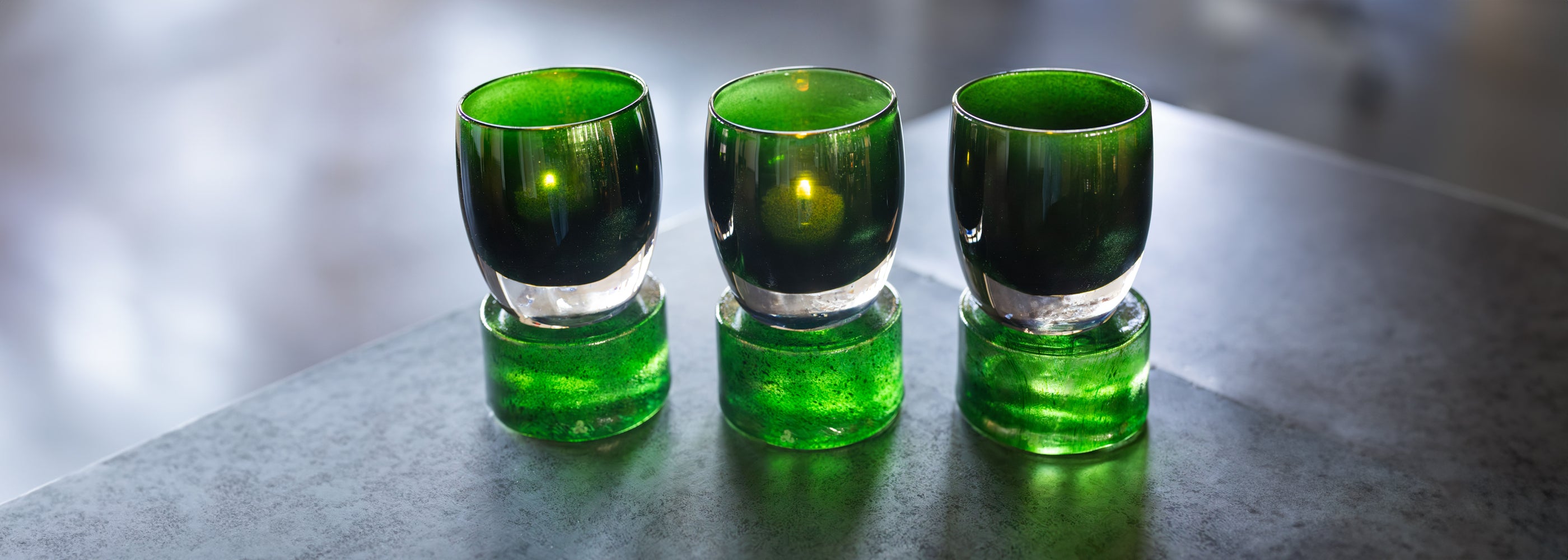 three robin hood green sparkle glassybaby hand-blown glass candle holders sitting on green pedestals. 