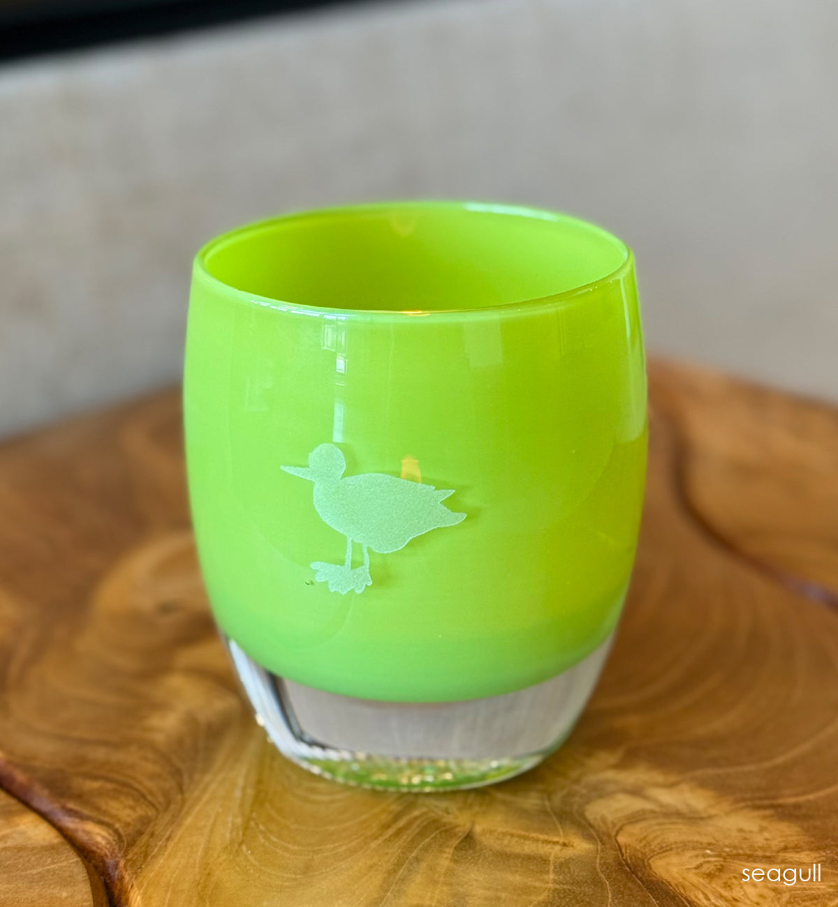 Green glass candle holder with a hand-etched seagull on a wooden surface