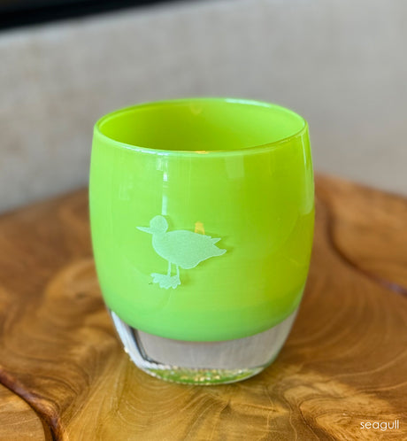 Green glass candle holder with a hand-etched seagull on a wooden surface