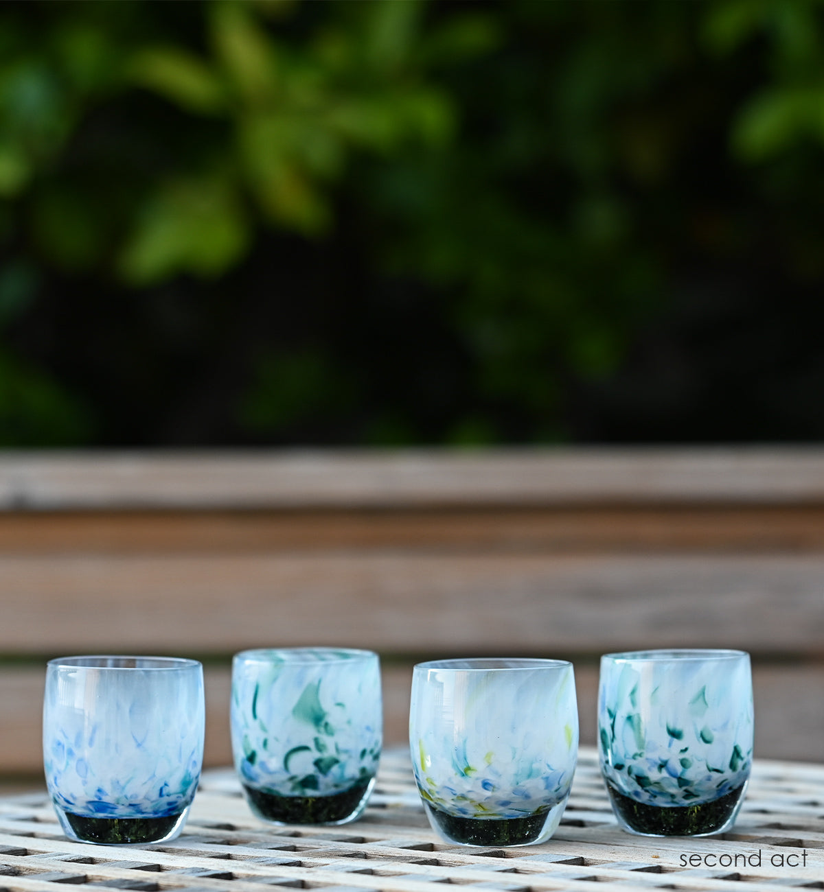 four second act hand-blown glass votive candle holders made from recycled glass from 43 colors, on a backyard patio table.