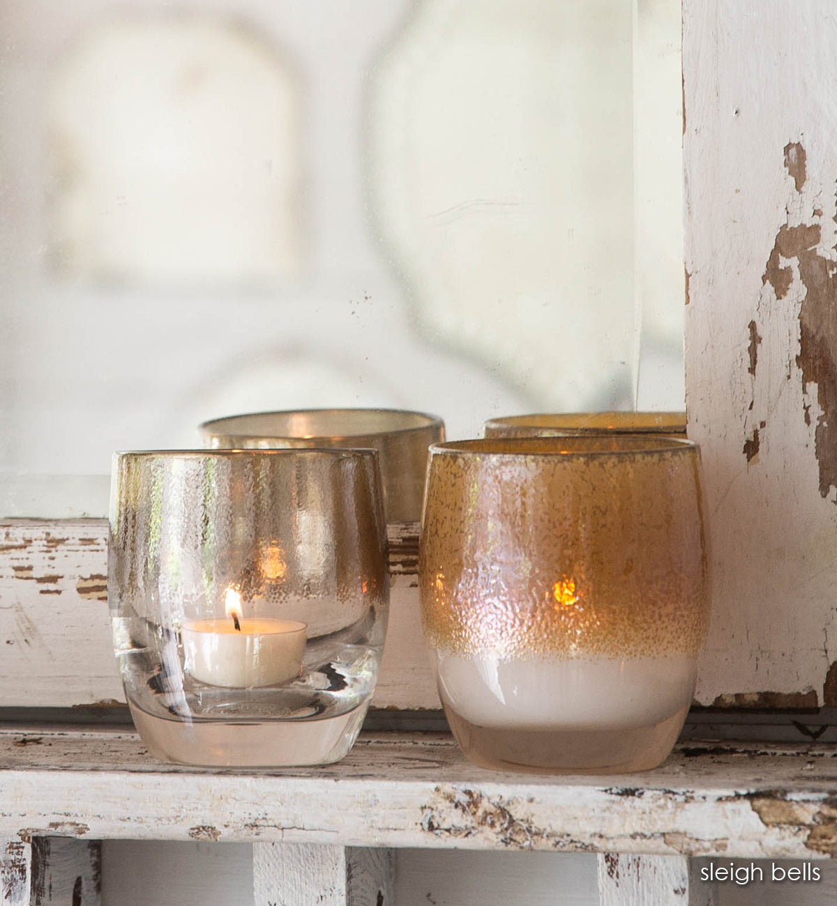 sleigh bells set, silver lining silver on clear, grace gold on white, hand-blown glass votive candle holders on wood shelf. 