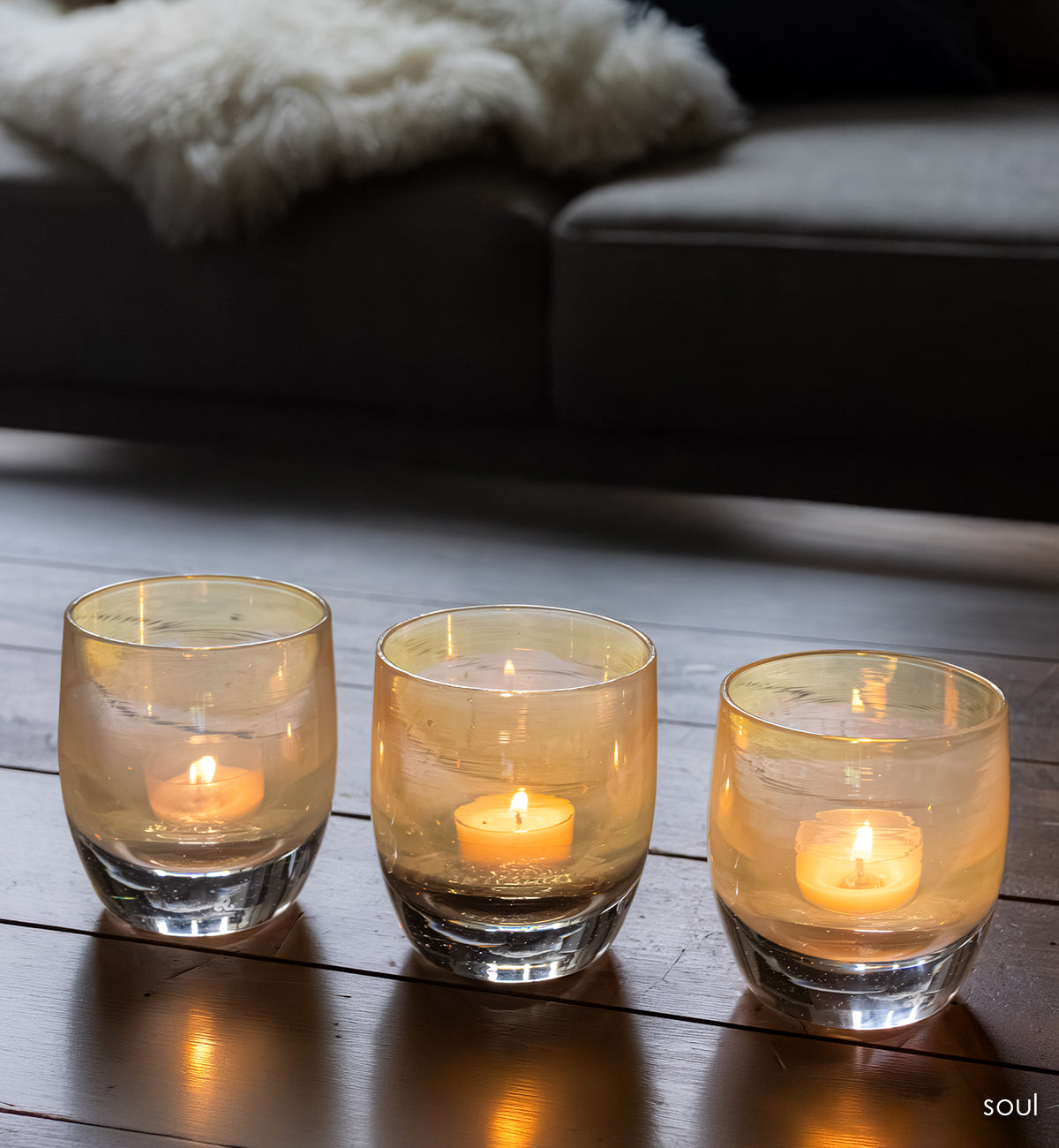 three 'sou' a light yellow transparent glass candle holders with a lit candle on woof table 