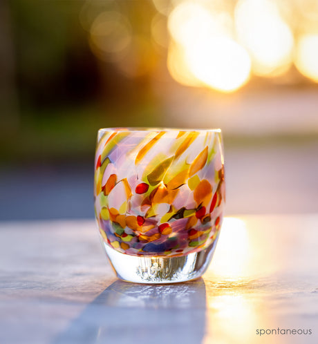 'spontaneous' colorful hand-blown glass candle holder with sunshine behind it
