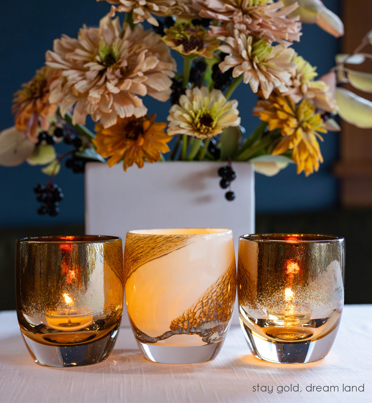 dream land, cream with brown textured swirls hand-blown glass votive glassybaby with two 'stay gold' glassybaby on each side with fall flowers in the background.
