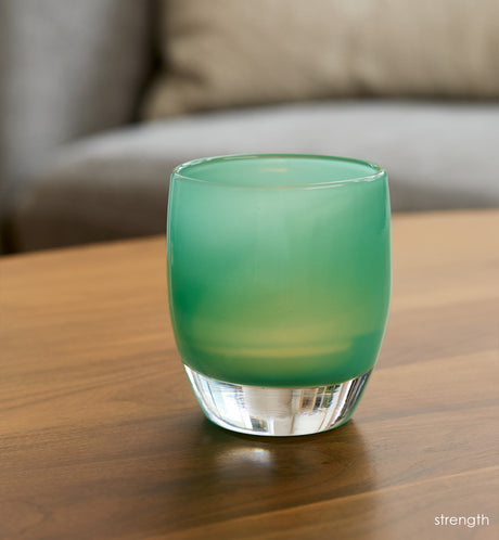 strength teal green hand-blown glass votive candle holder on a wood coffee table with gray couch in background.