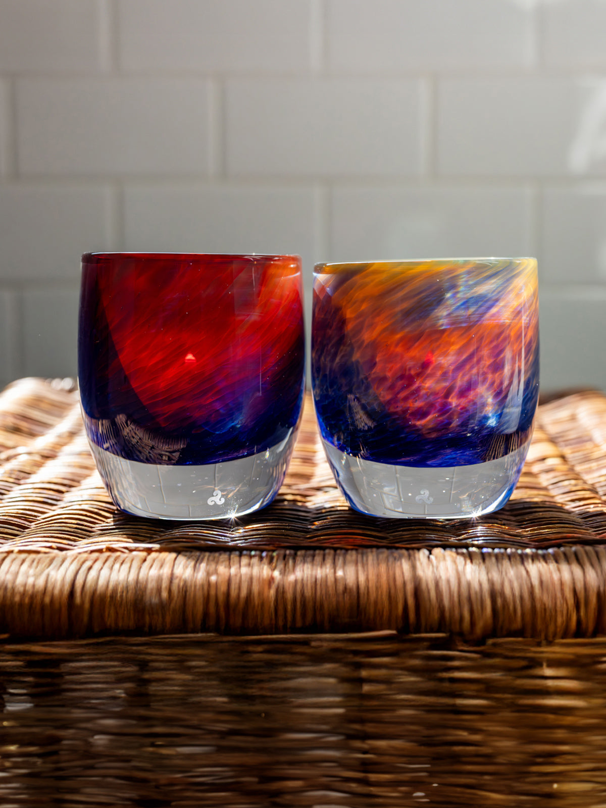 group of 'summer sunset' glassybaby red, blue, yellow hand-blown glass candle holder sitting wicker basket with white tile in the background.