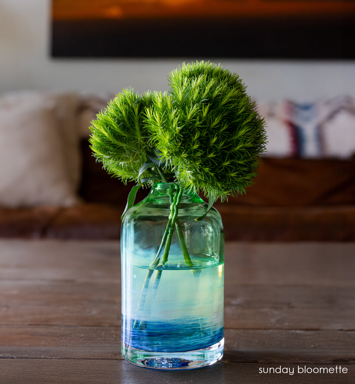 glassybaby bloomette transparent glass vase with blue and white accents on a wooden table with flowers inside the vase