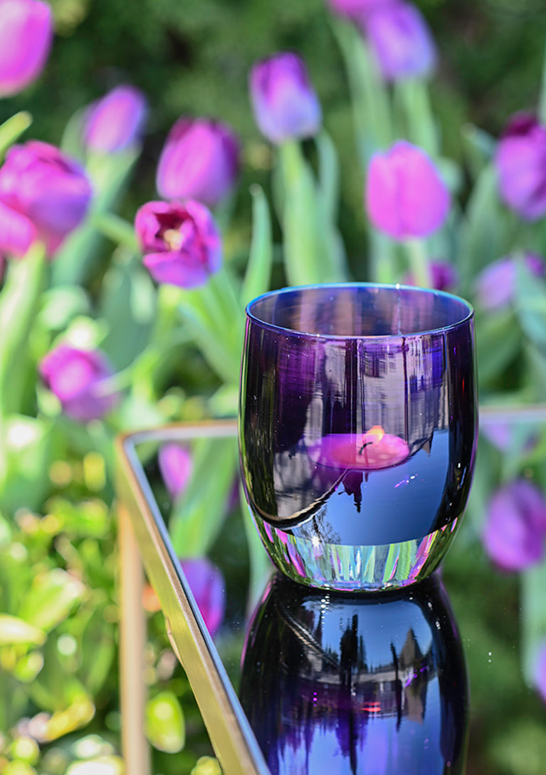 tulip, beautiful deep purple hand-blown glass votive with an iridescent inside sitting on a table in a field of tulips.