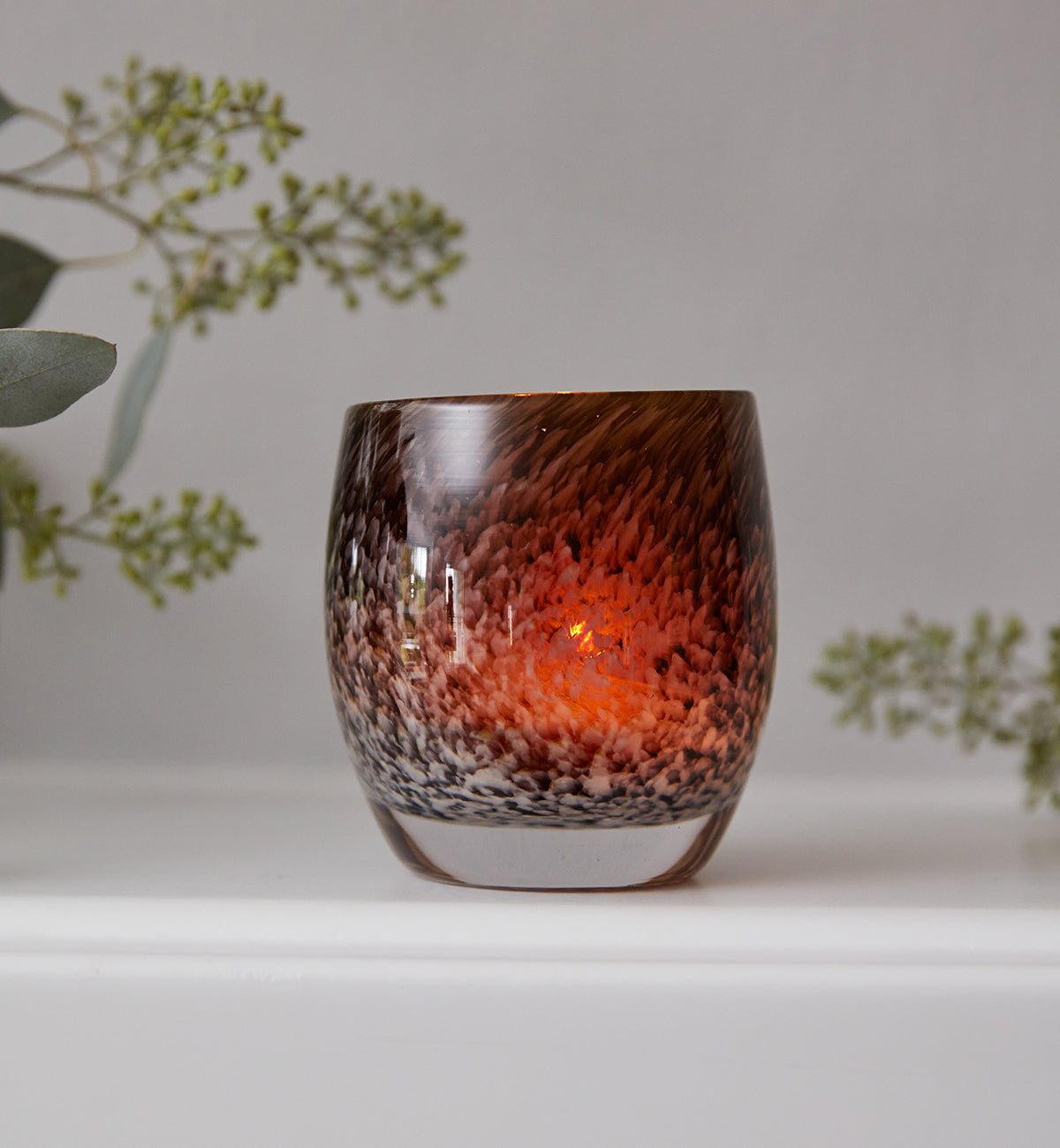 under a wing, an amber and brown mottled hand-blown glass candle holder.
