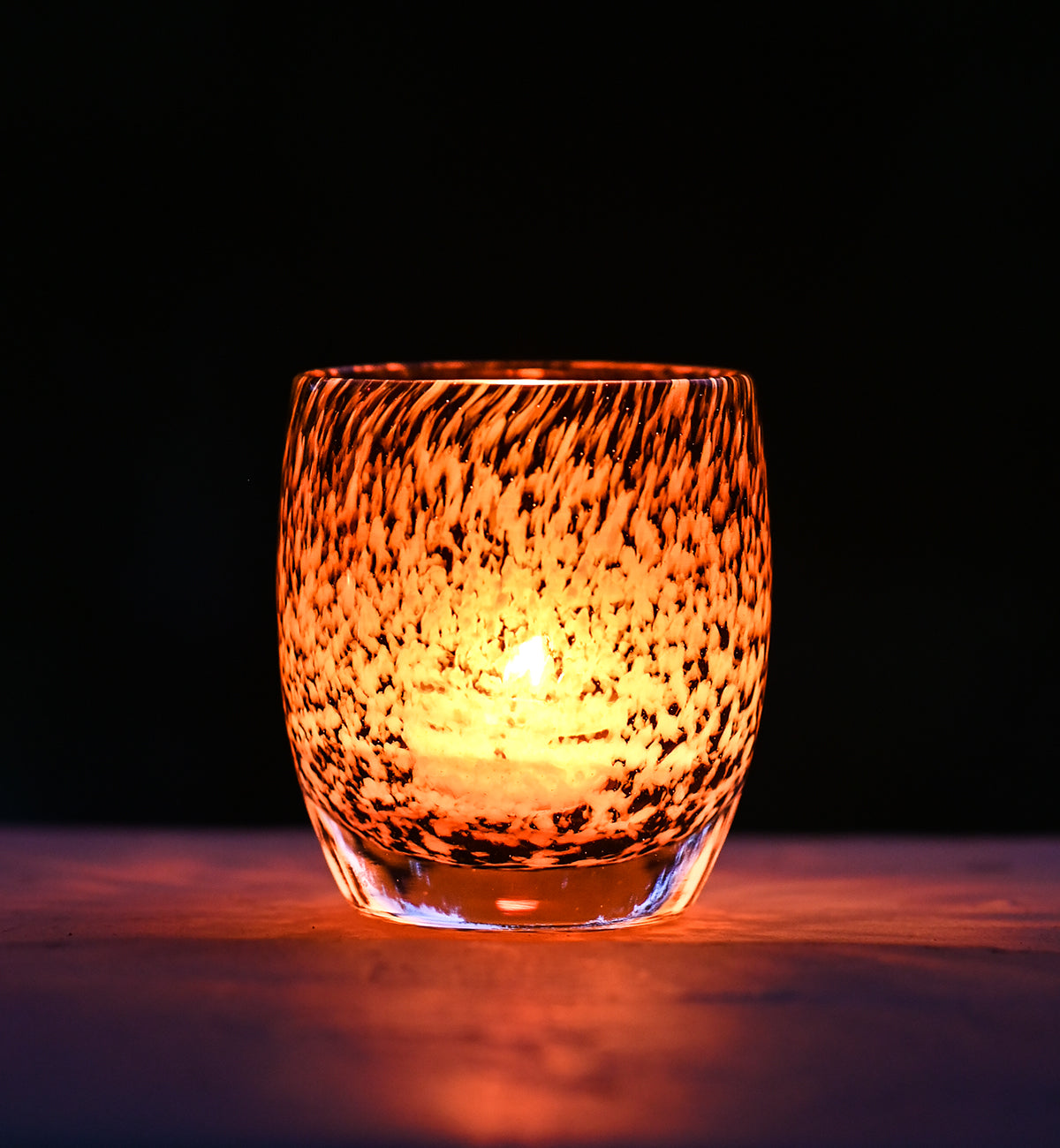 under a wing, an amber and brown mottled hand-blown glass votive candle holder.
