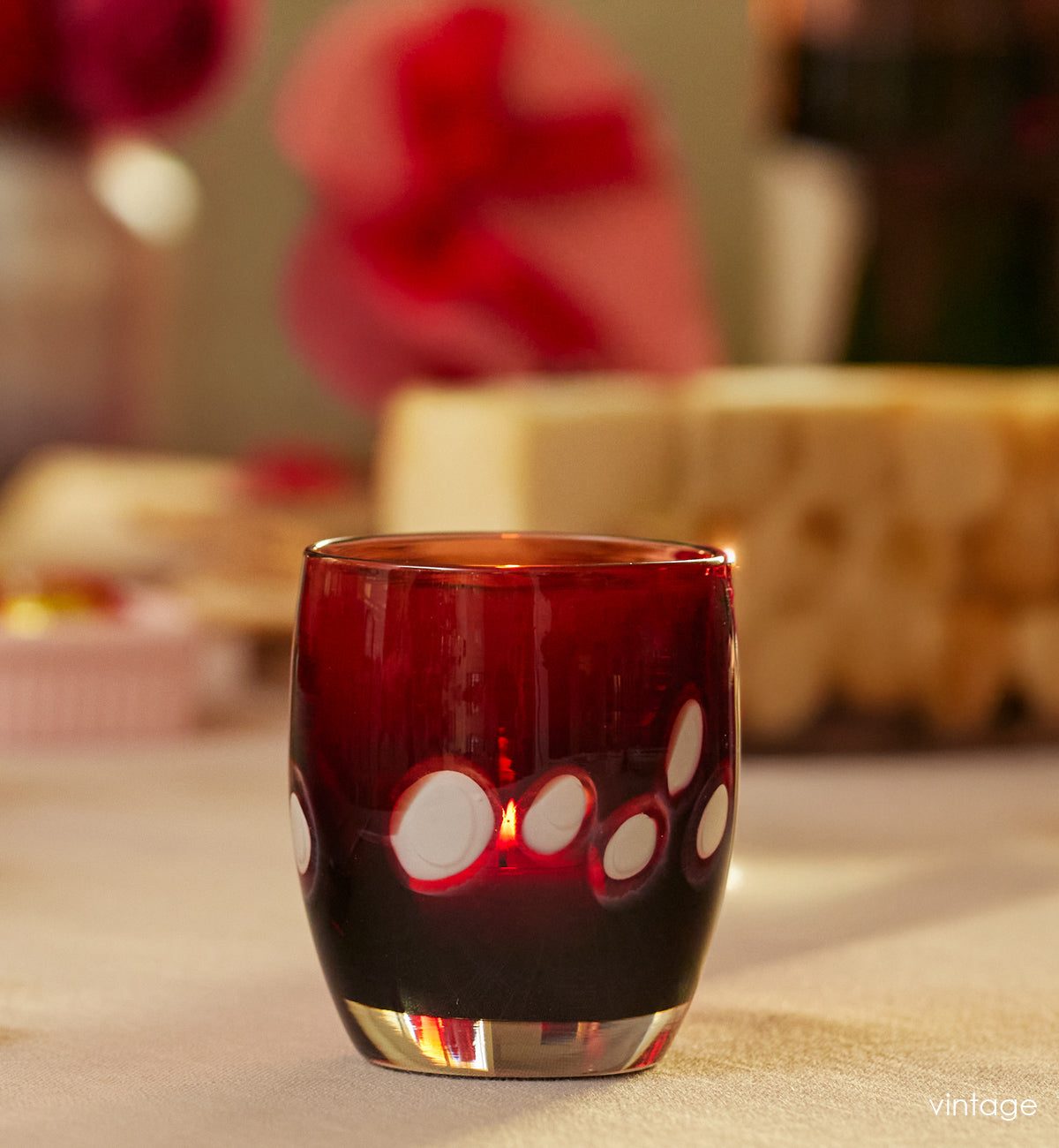 vintage red with white spots hand-blown glass candle holder with  pink roses on cream table cloth. 