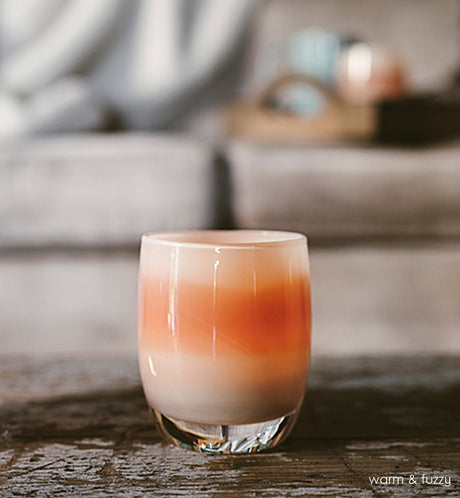 warm and fuzzy, cream glass with burnt orange stripe, hand-blown glass votive candle holder on a wood coffee table with couch blurred in background.