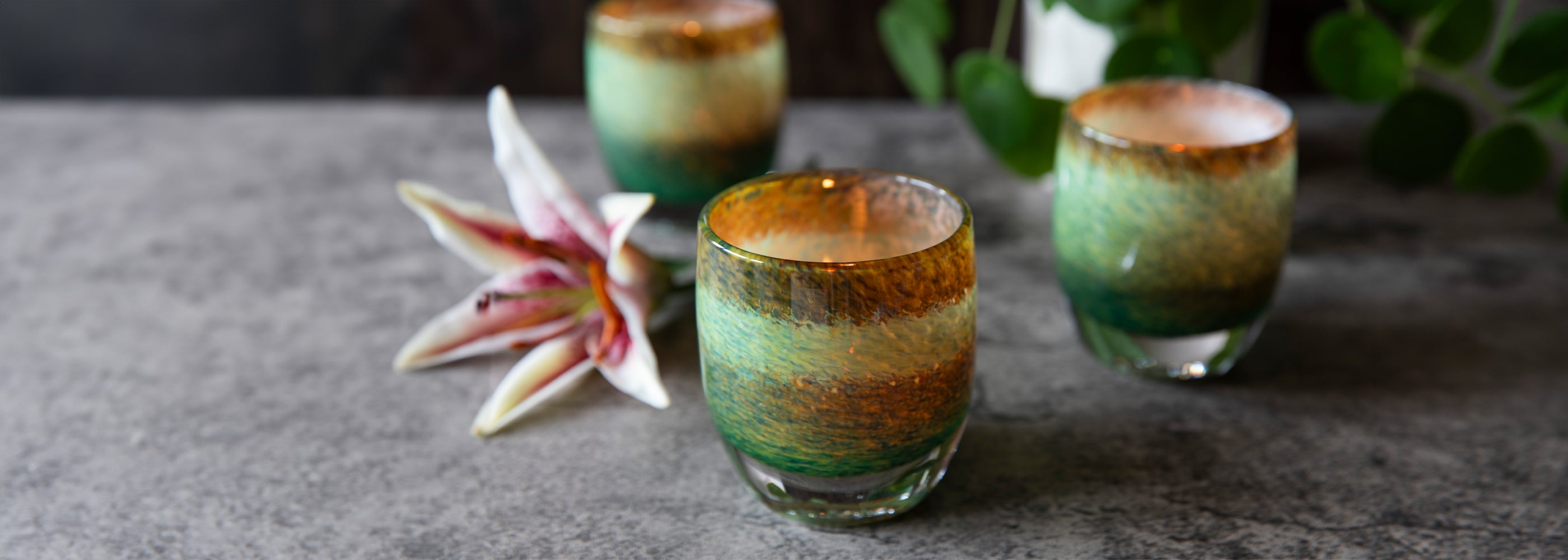 Decorative glass candle holders with a green gradient color on a textured surface.
