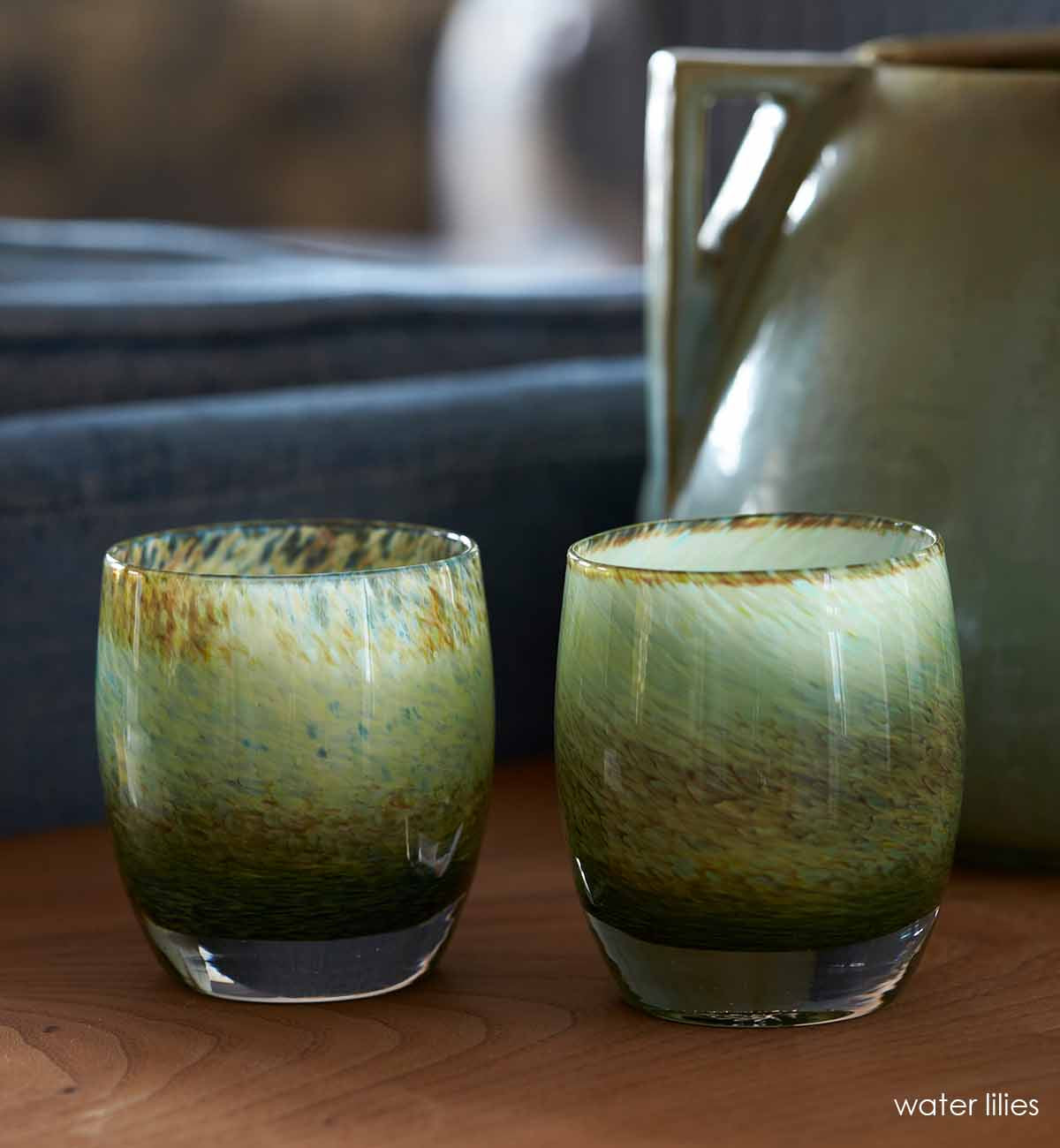 two water lilies pond green hand-blown glass votive candle holders on a wooden living room side table.