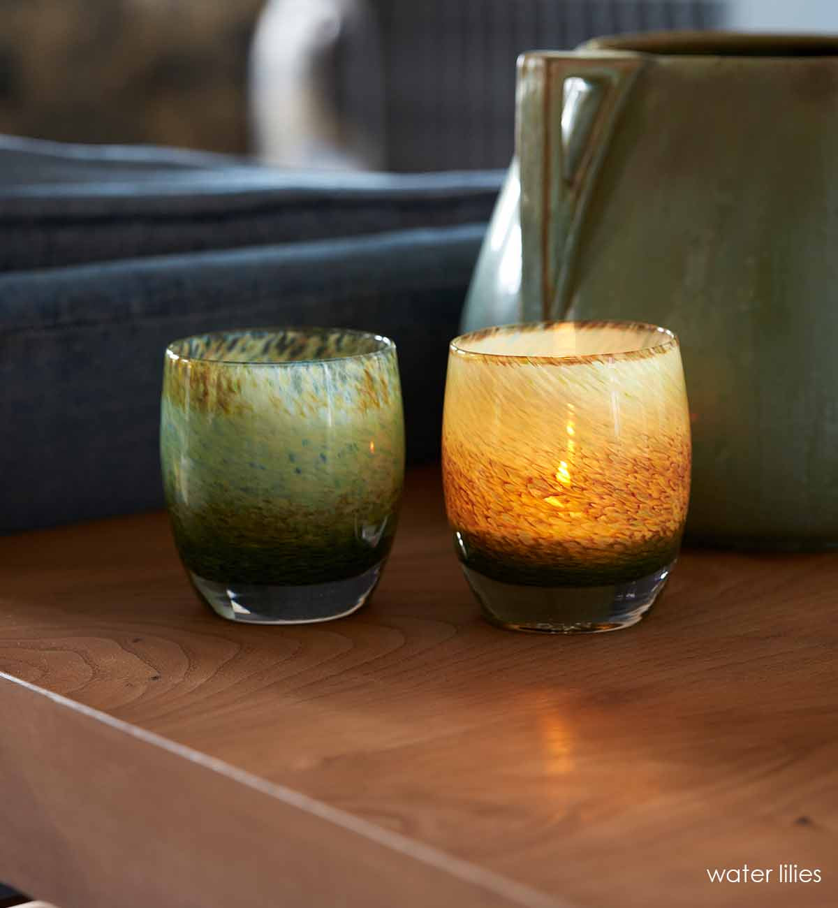 two water lilies, garden pond earthy green blue textured hand-blown glass votive candle holders sitting on a light wood table next to a blue couch.