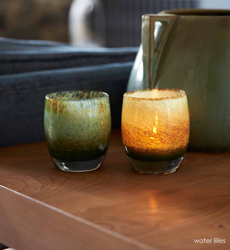 two water lilies, garden pond earthy green blue textured hand-blown glass votive candle holders sitting on a light wood table next to a blue couch.