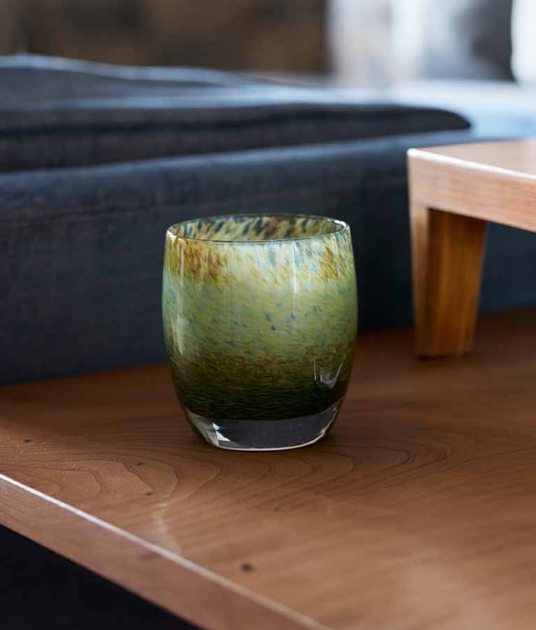 A green pond texture water lilies sit on a wooden side table. Hand-blown glass votive candle holders.