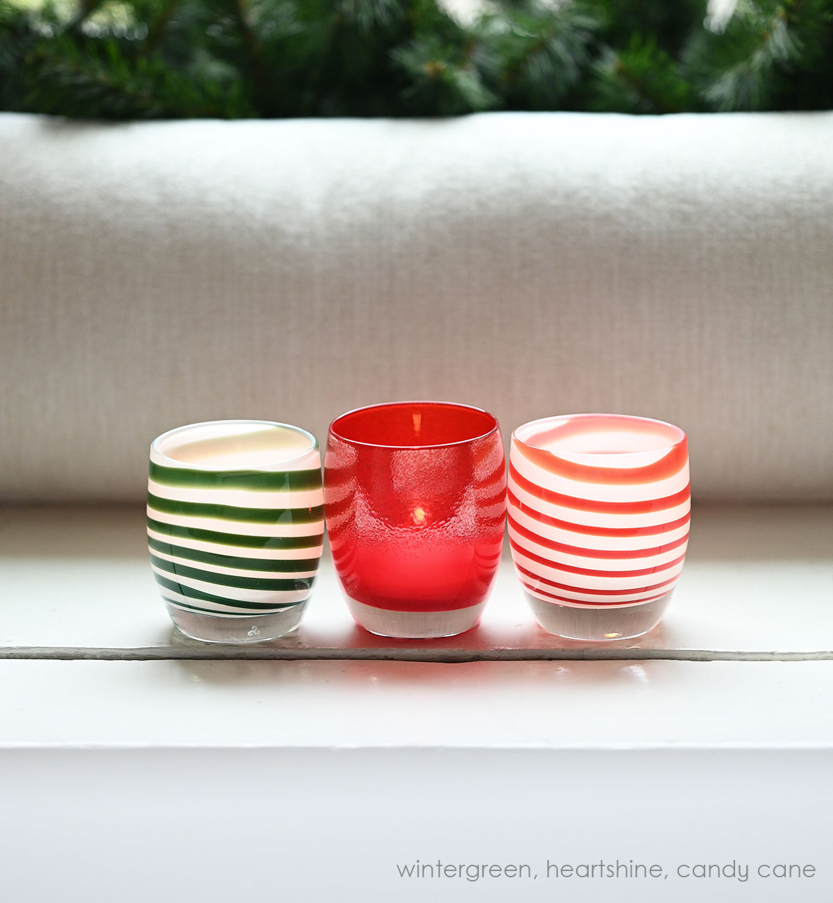 green stripes on a white base create beautiful wintergreen, a hand-blown glass votive candle holder placed with heartshine and candy cane on a cream mantle and evergreen branches behind.