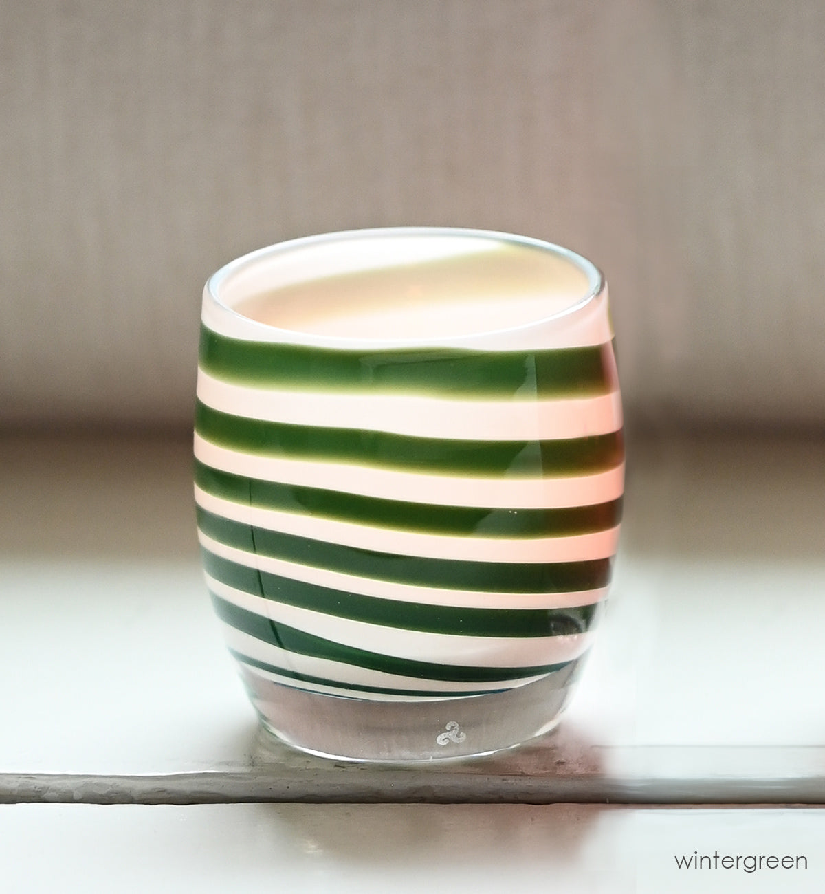 green stripes on a white base create beautiful wintergreen, a hand-blown glass votive candle holder with a lit tealight on a white table