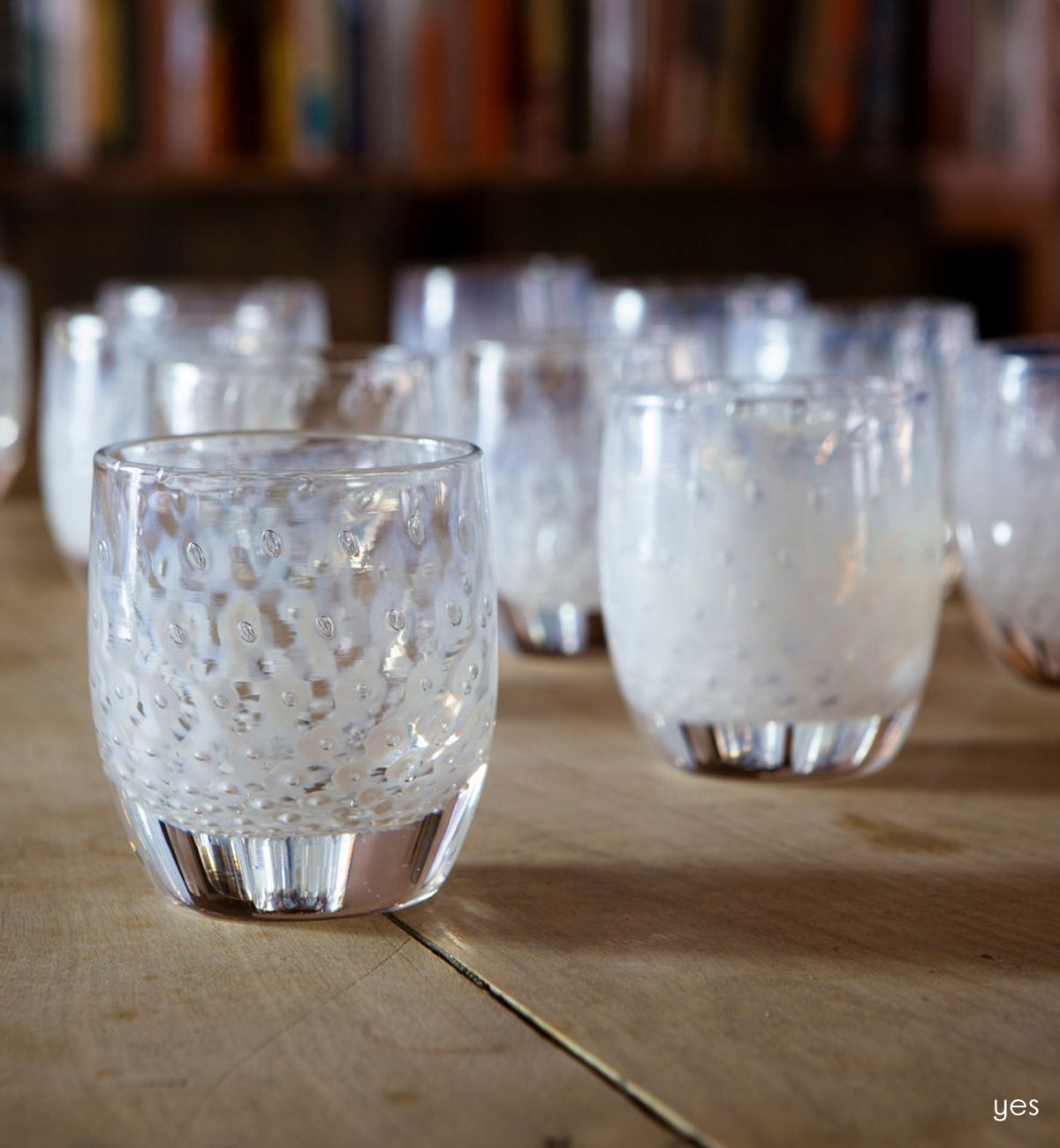 grouping of yes, white unique bubble pattern hand-blown glass votive candle holders on a light wood table with bookshelves behind.