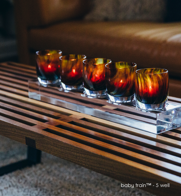 five well acrylic baby train with five lucky penny on a wood ottoman with brown leather couch in background.