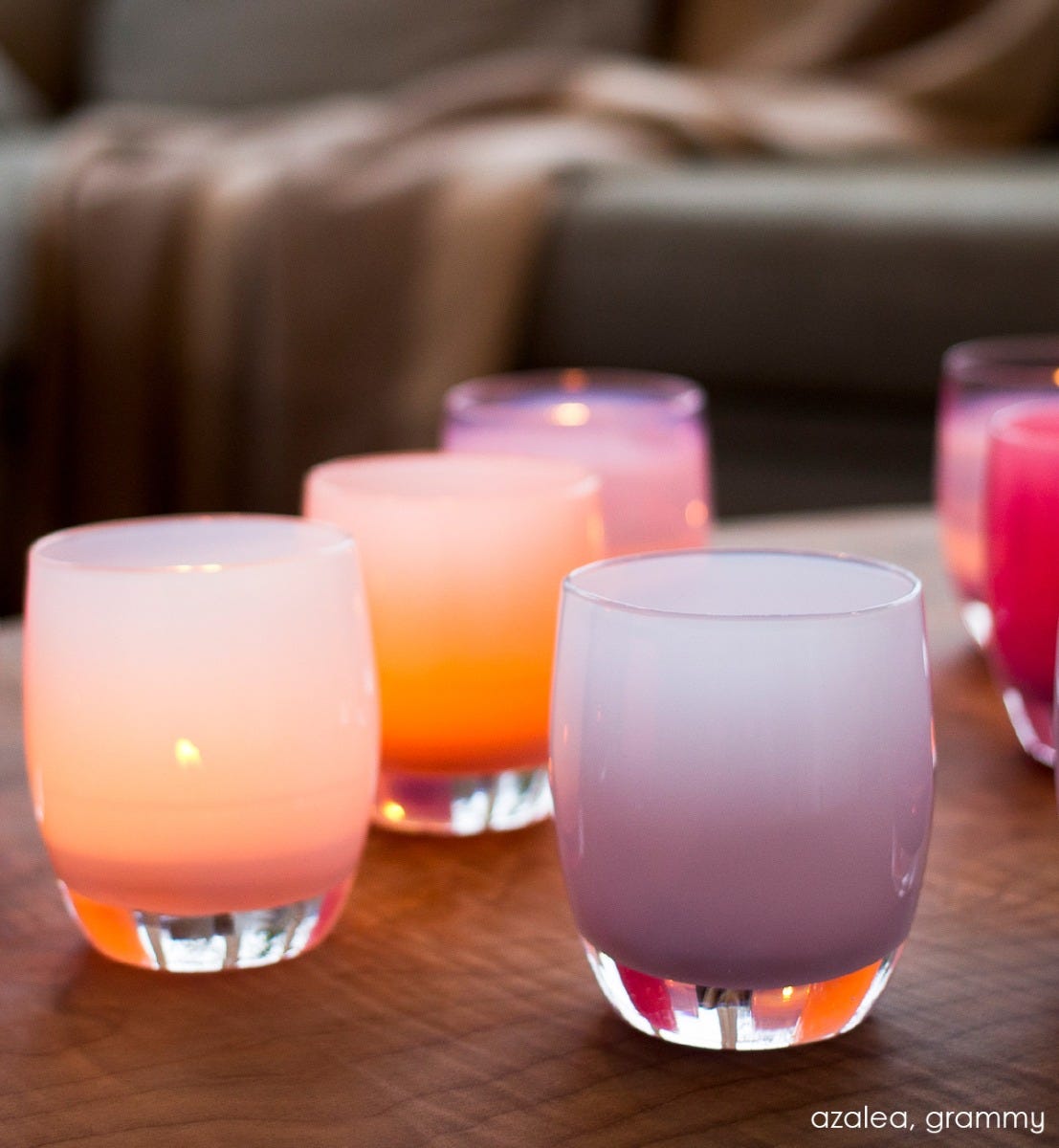 azalea light pink hand-blown glass votive candle holder next to grammy on a brown leather living room ottoman.