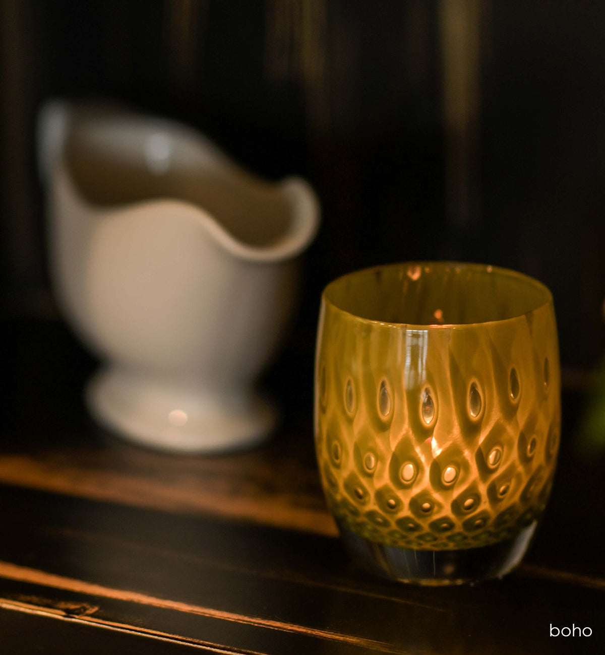 boho olive green bubble hand-blown glass votive candle holder on a wood table next to a cream vase.