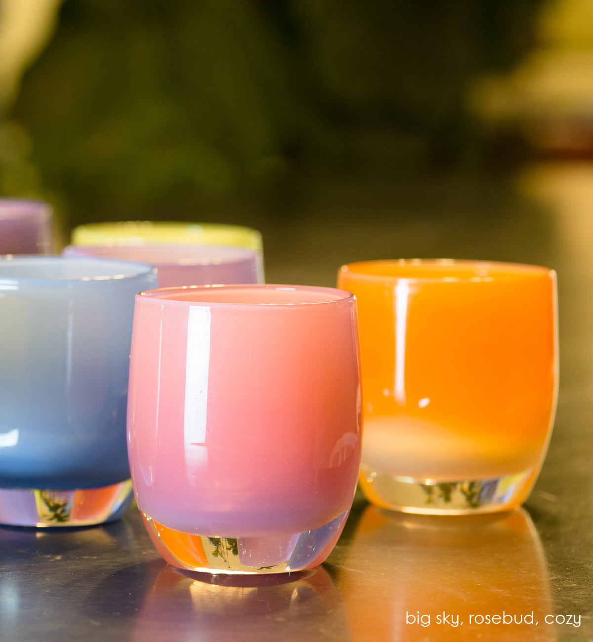 cozy, stripey apricot orange hand-blown glass votive candle holder, paired with big sky and rosebud on a reflective surface.