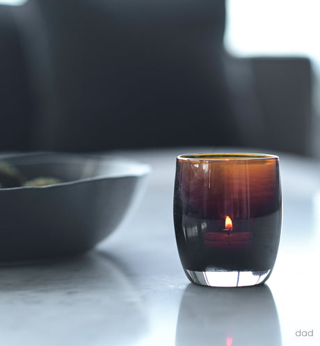 dad translucent dark brown hand-blown glass votive candle holder on marble living room table next to decorative bowl.