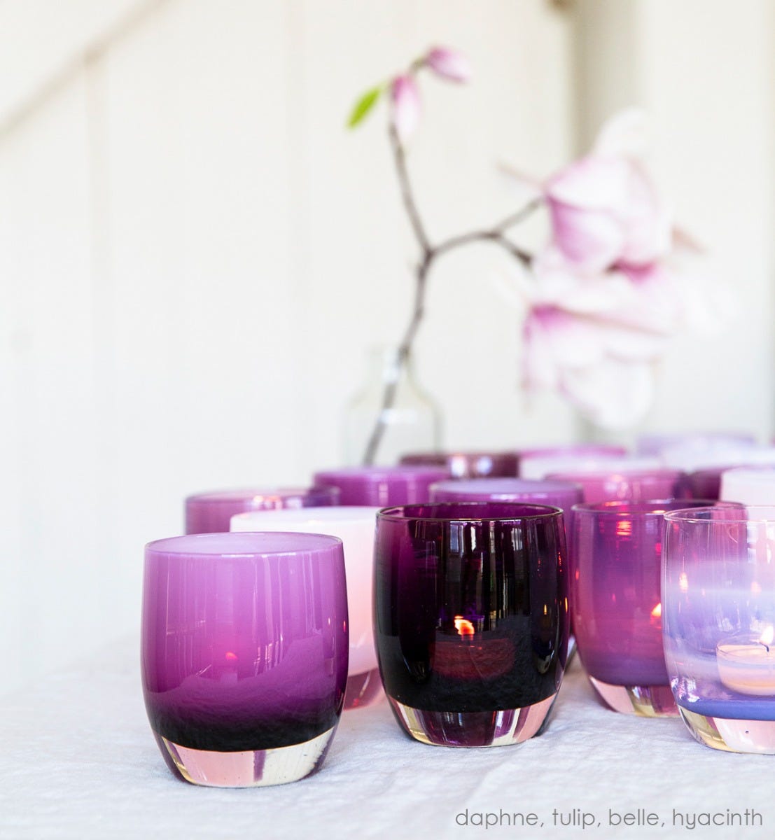 daphne bright purple with white interior, hand-blown glass votive candle holder. Paired with tulip, belle, and hyacinth on cream tablecloth.