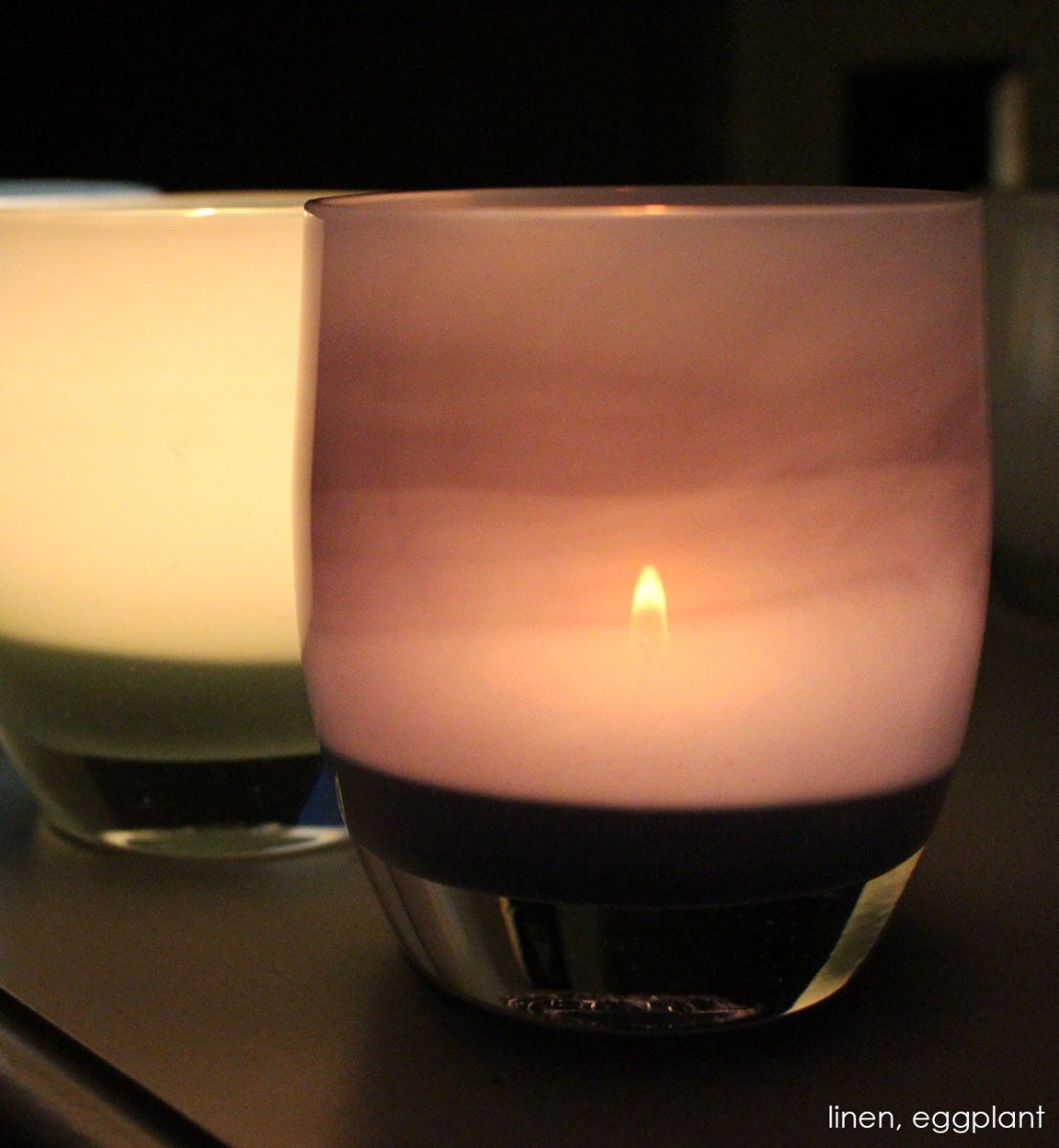 eggplant purple glass hand-blown glass votive candle holder. Paired with linen on a dark surface.