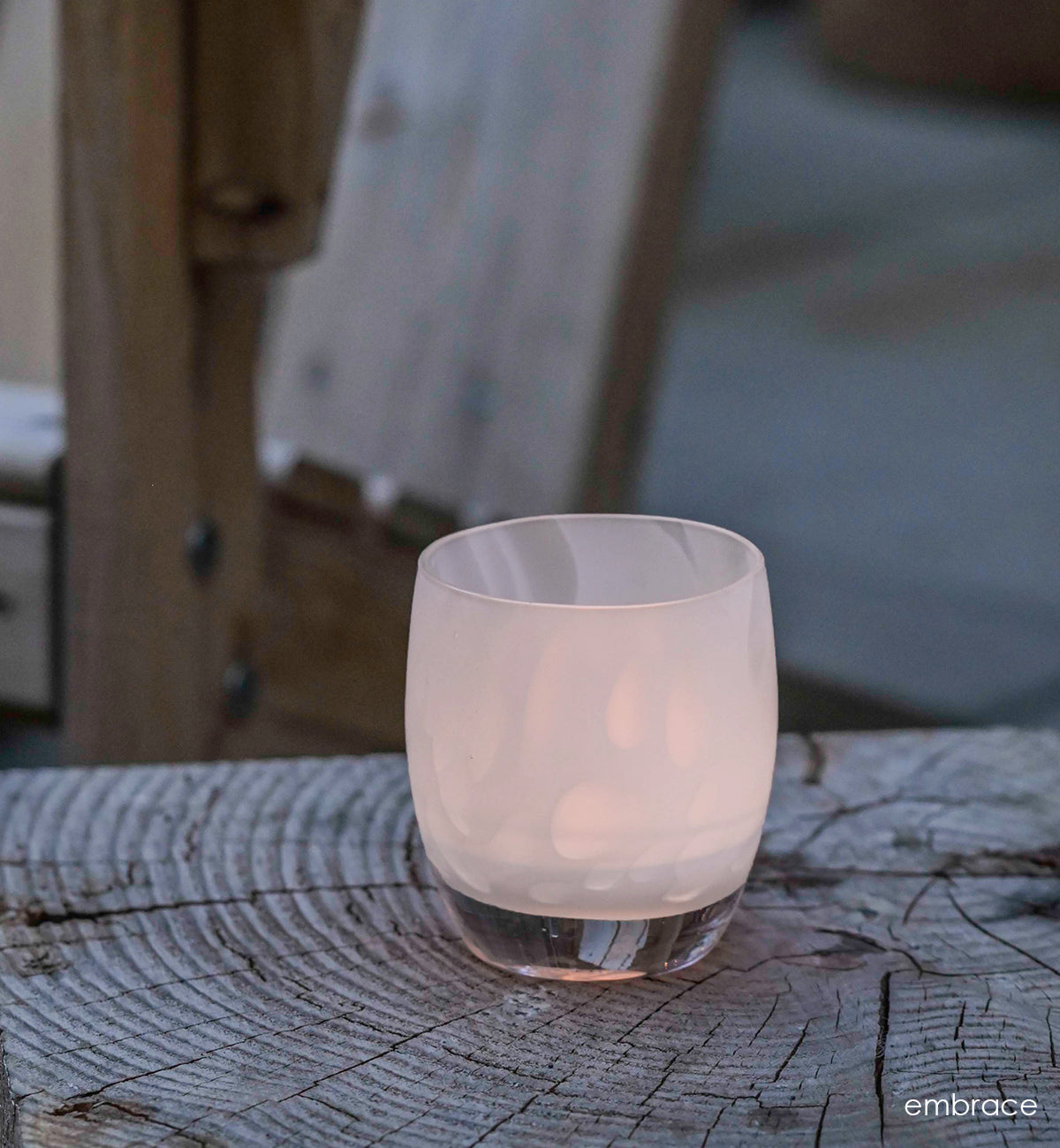 embrace white with petal, hand-blown glass votive candle holders on a wood stump with a wood chair in background.
