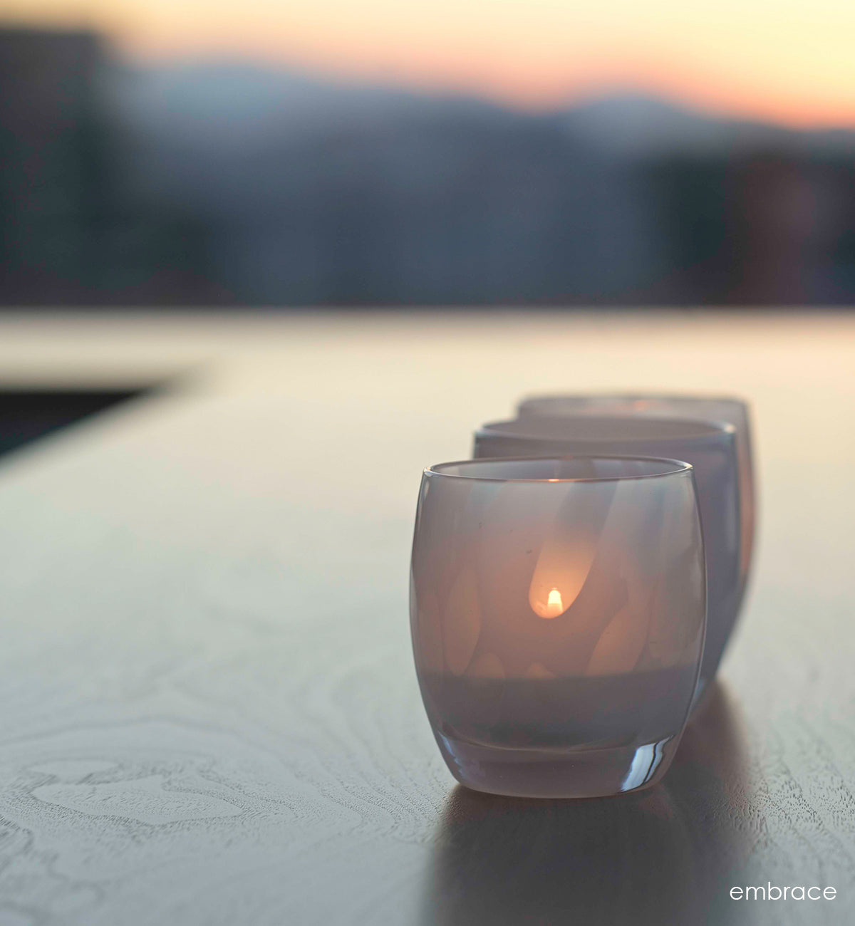 two embrace white with petal, hand-blown glass votive candle holders on a table overlooking the sunset.